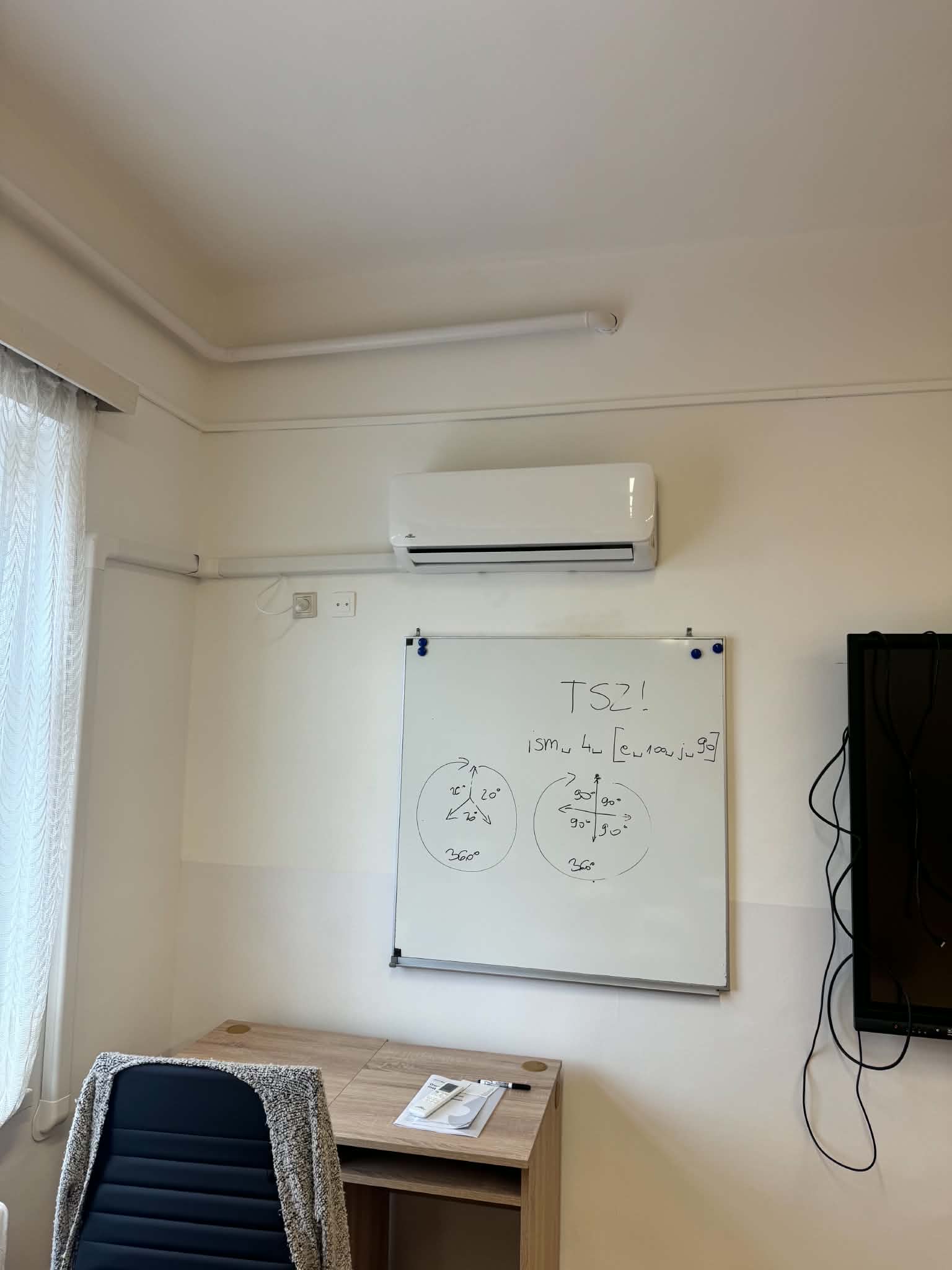 Beltéri klímaegység egy iroda falán, alatta írótáblával és íróasztallal