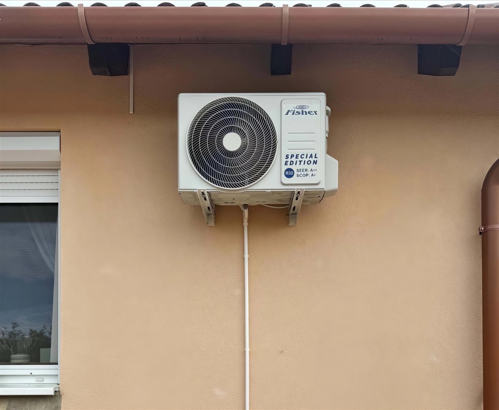 Kültéri klímaegység egy családi ház barna homlokzatán, az eresz alatt
