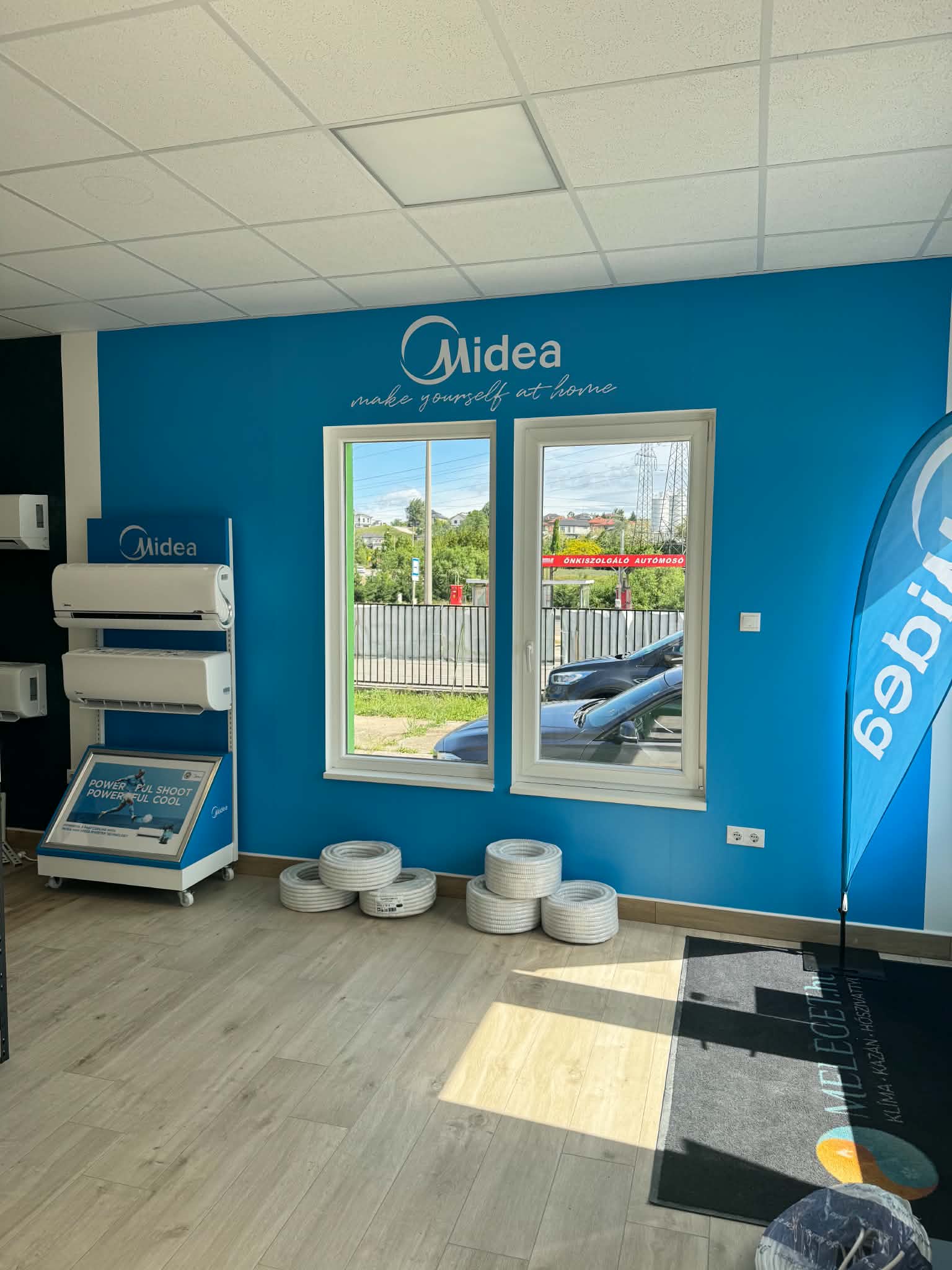 Beltéri klímaegységek és bemutatóállványok az üzlet Midea feliratú kék fala mellett